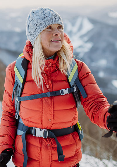 a woman in her 60s wearing a red jacket and hiking a snow covered mountain top